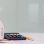 Maison en papier avec à côté d'un crayon et d'une calculatrice
