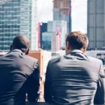 Deux hommes assis de dos avec des grattes-ciels en face d'eux