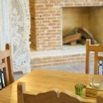 ne table de salle à manger en bois massif avec des bougies décoratives, devant une cheminée en briques rustique et un paravent blanc sculpté.