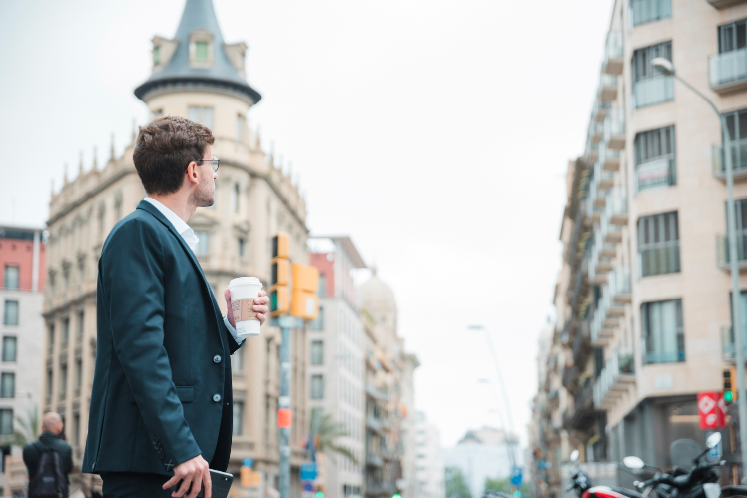 un homme en costume élégant, tenant un café à emporter, observe l'architecture d'une grande avenue européenne