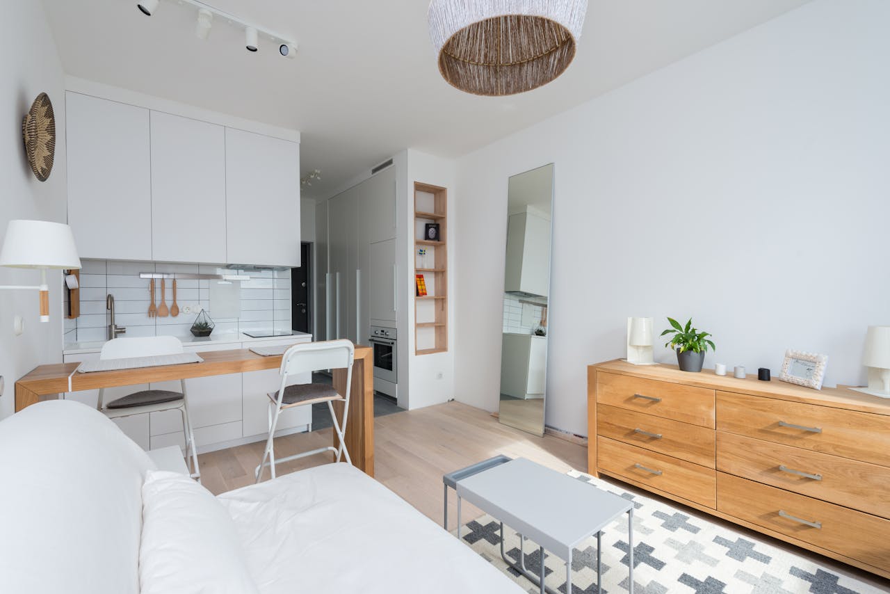 Cosy Home et les nouvelles tendances de la location meublée à Paris en 2026 Un studio de style scandinave avec une cuisine blanche intégrée, une table haute en bois servant de bar, un canapé blanc et une commode en bois clair