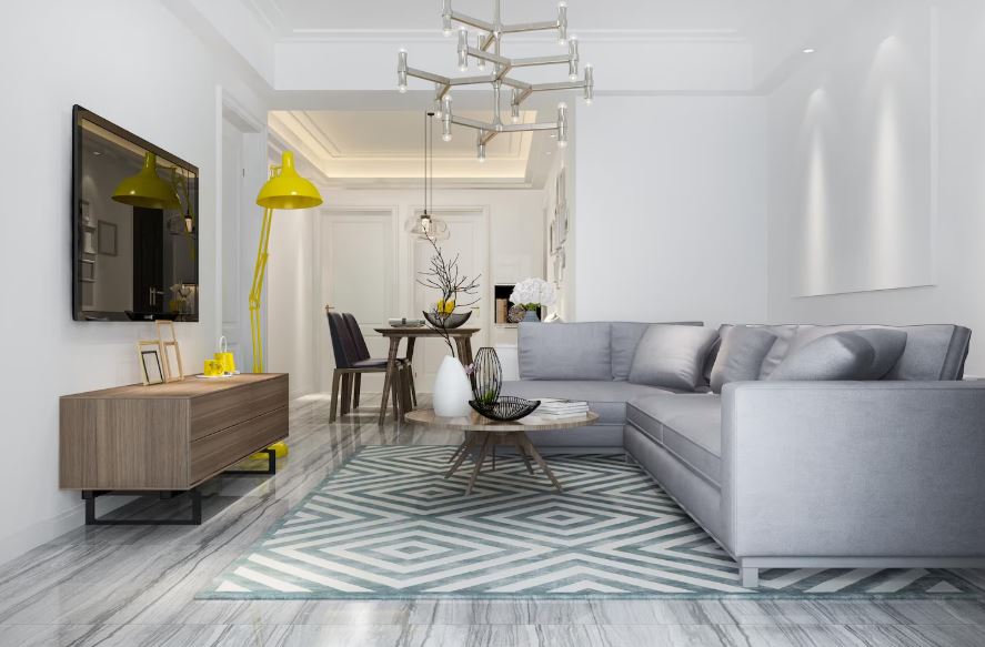 Un salon moderne et lumineux aux tons blancs et gris, doté d'un grand canapé d'angle, d'un tapis à motifs géométriques bleus et d'un grand lampadaire jaune vif.