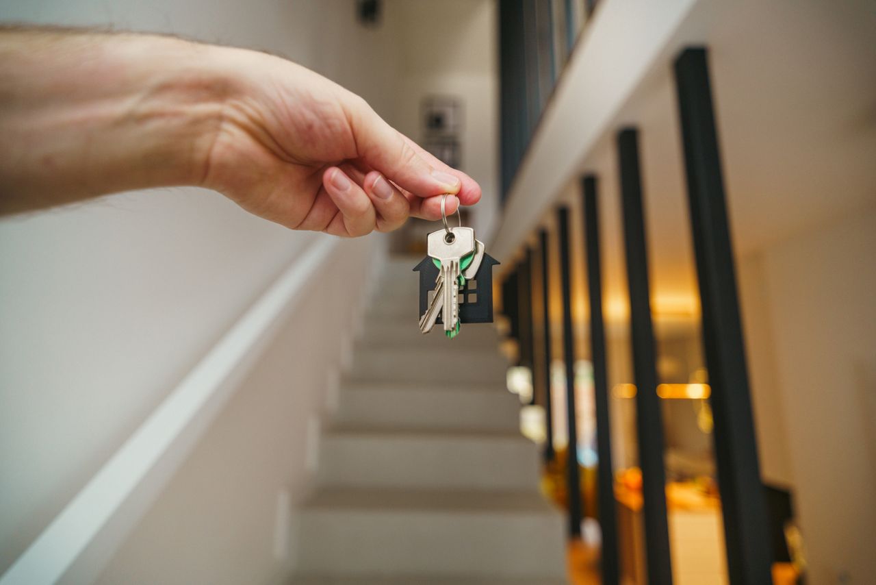 une main tenant un trousseau de clés avec un porte-clés en forme de maison